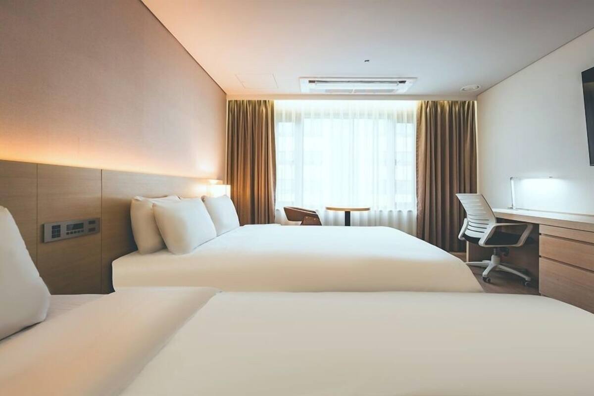 Une chambre d’hôtel avec deux lits, un bureau, une chaise, une télévision et une fenêtre avec des rideaux.