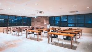 Ein Konferenzraum mit mehreren Tischen und Stühlen, großen Fenstern und einem Projektor an der Decke.