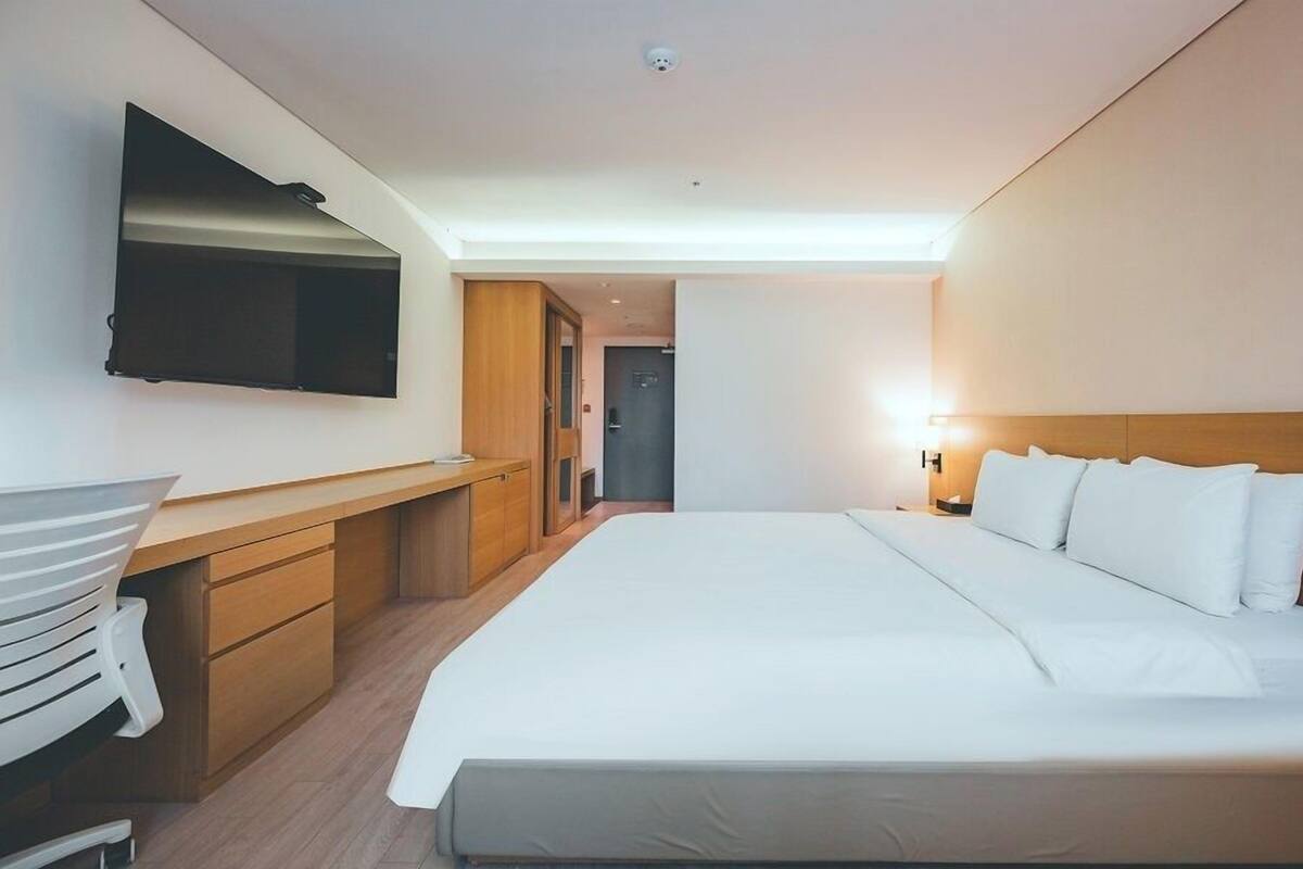 Une chambre d’hôtel avec un grand lit, un bureau doté d’un téléviseur à écran plat et une table de chevet en bois.