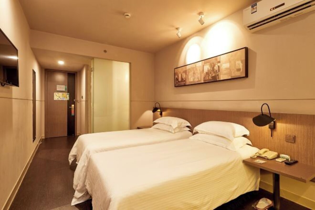 Habitación de hotel con dos camas, una mesita de noche con lámpara, aire acondicionado instalado en la pared y un cuadro enmarcado.