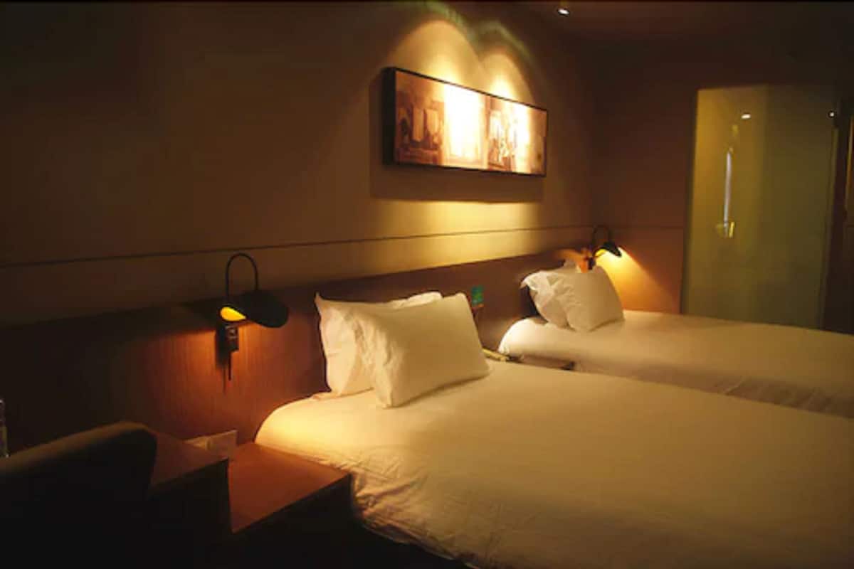 Una habitación de hotel con dos camas, una mesita de noche, una lámpara y un cuadro en la pared.