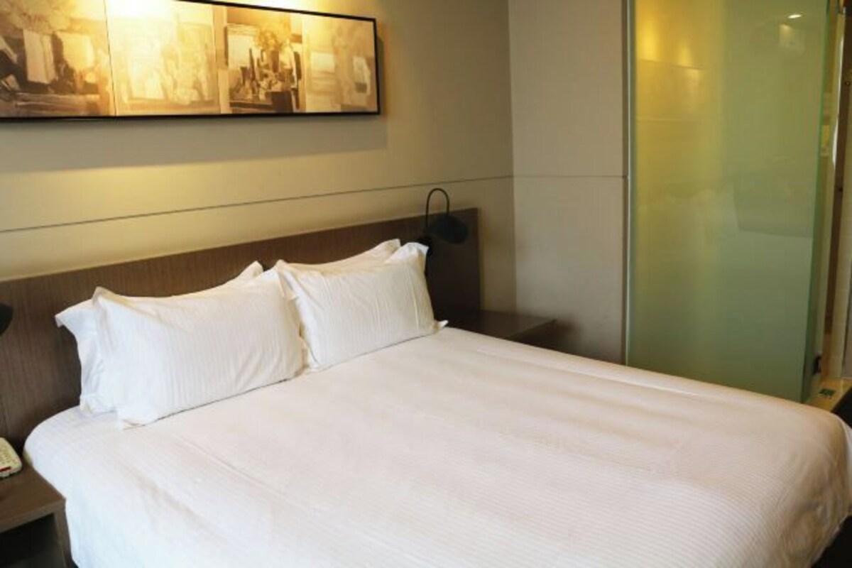 Una habitación de hotel con una cama grande, una mesita de noche con una lámpara y una obra de arte en la pared.