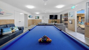 A pool table with balls, a sofa, and a television in a room with a ceiling fan and a door leading outside. - Motel Sunshine Coast (Caloundra)