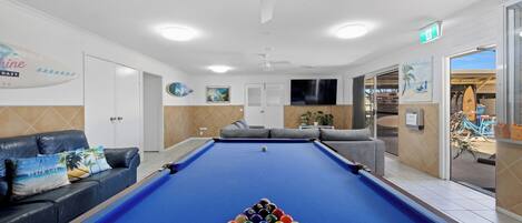 A pool table with balls, a sofa, and a television in a room with a ceiling fan and a door leading outside.
