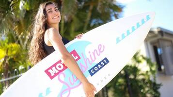 Een persoon die een surfboard vasthoudt, waarop 'Motel Sunshine Coast' staat.