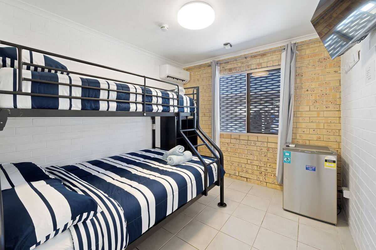 A bunk bed with striped bedding, a small refrigerator, and a window with blinds.