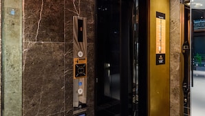 Um elevador com parede de mármore, sinal de código de andar e sinal de acessibilidade para cadeiras de rodas.