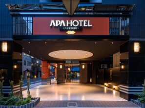 The exterior of APA HOTEL with a modern design, featuring a prominent entrance and a clear view of the lobby area.