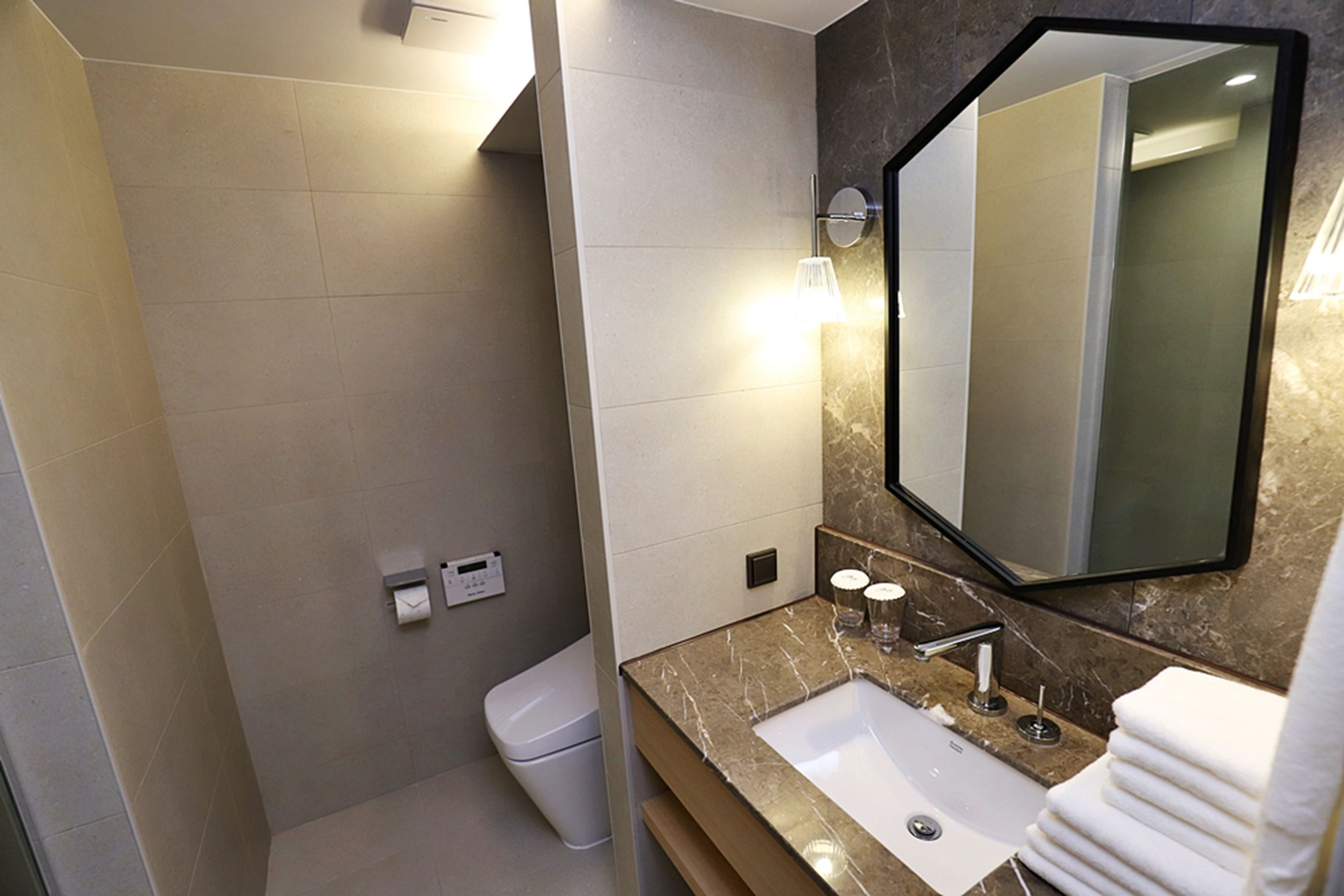 A modern bathroom with a marble sink, a large mirror, and a toilet.