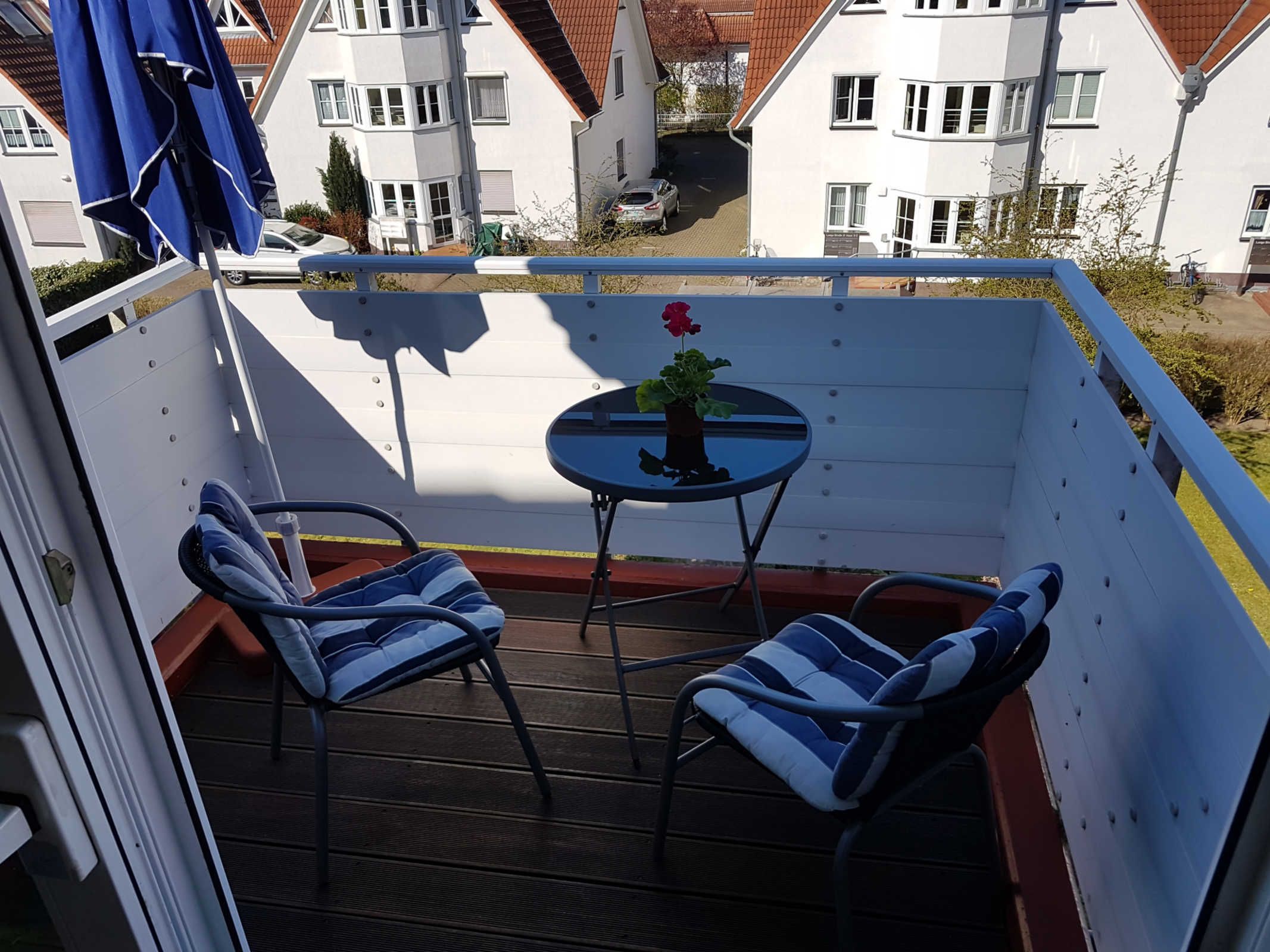 En balkon med to stole, et lille bord med en potteplante og en blå parasol.