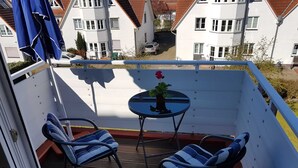 Un balcón con dos sillas, una mesita con una planta en maceta y un paraguas azul.