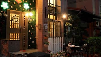 A building entrance with a green wall decorated with flowers and a sign above the door. There is a small outdoor seating area with a table and chairs.