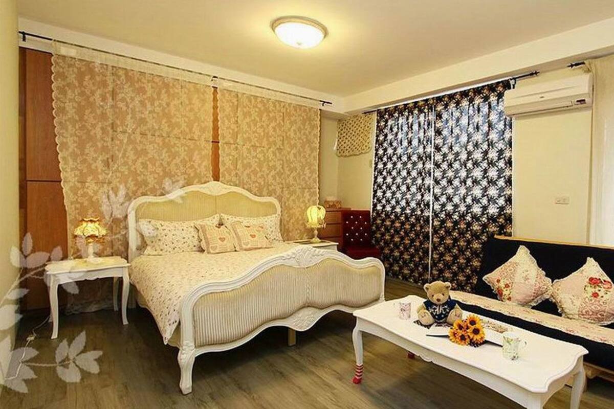 A bedroom with a bed, bedside tables, a sofa, and a decorative teddy bear.