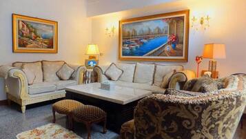 A living room with a sofa, armchair, and coffee table, with two paintings on the wall and a lamp on the side.