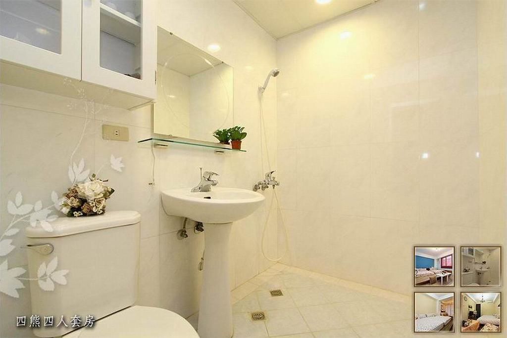 A bathroom with a toilet, sink, and shower. There is a mirror above the sink and a shelf with a plant. The walls are tiled and the floor is tiled.