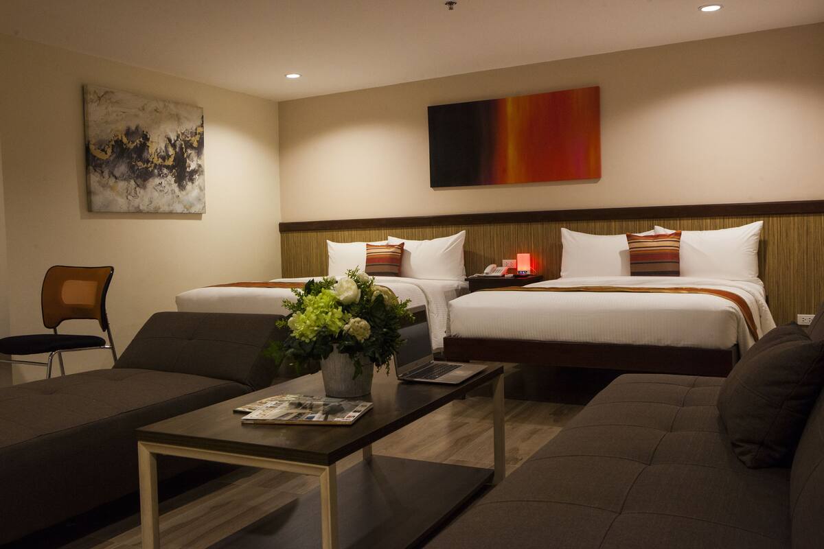 A hotel room with two beds, a sofa, a coffee table, and a painting on the wall.
