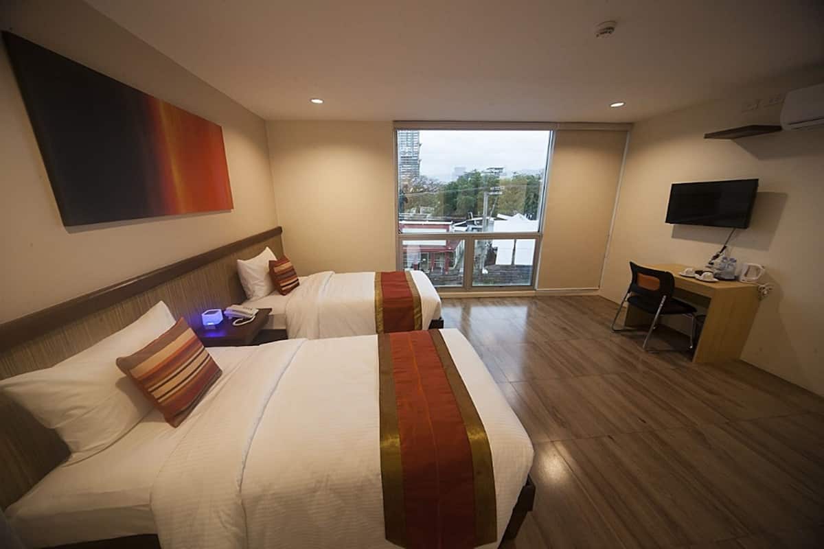 A hotel room with two beds, a desk, and a TV.