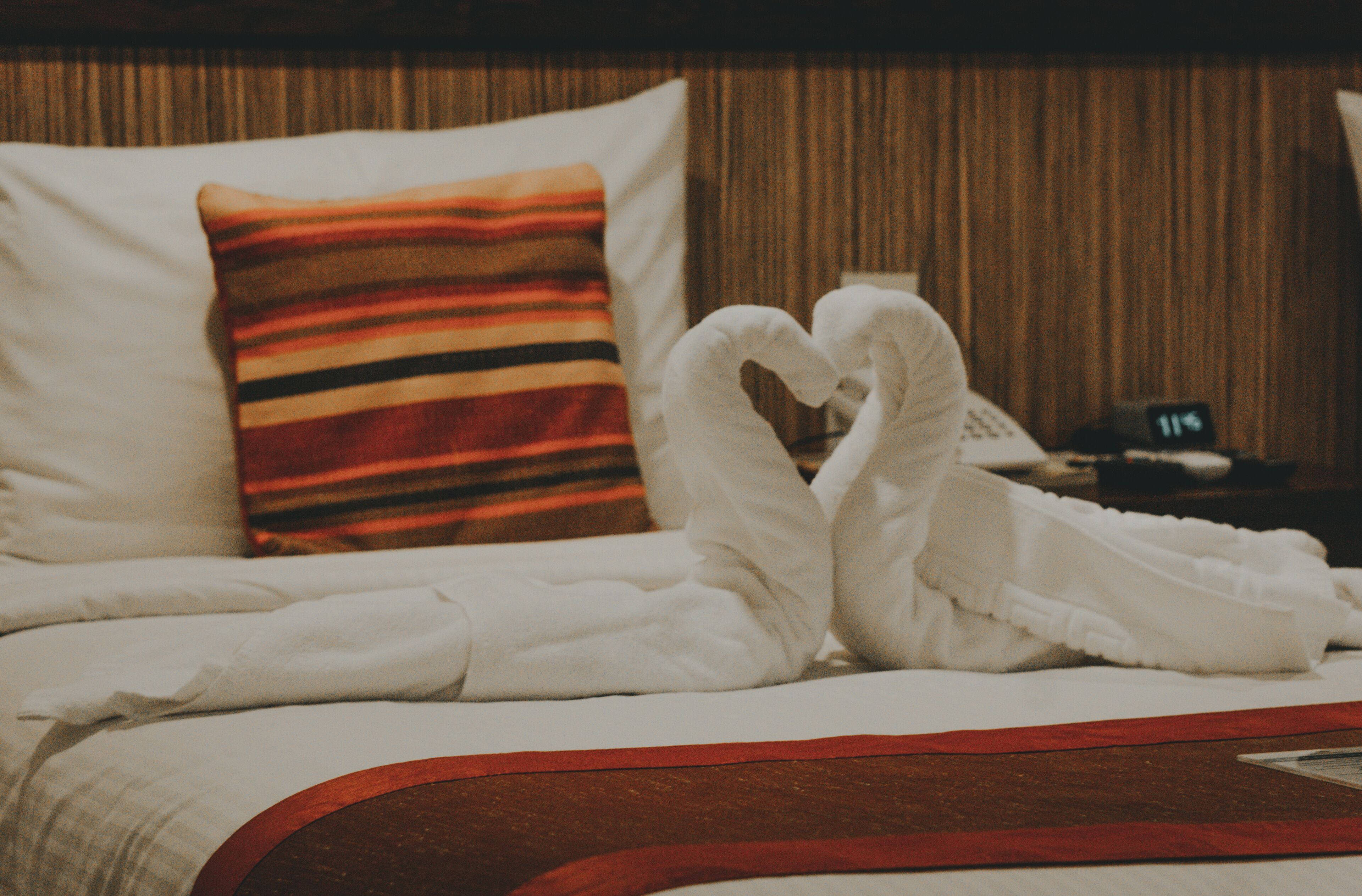 Habitación de hotel con una cama, almohada a rayas y toallas blancas dispuestas en forma de corazón.