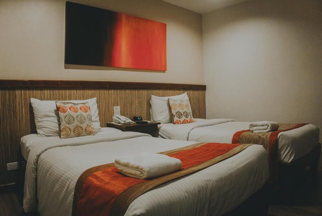 A hotel room with two beds, a wooden headboard, a red abstract painting, and a telephone on the nightstand.