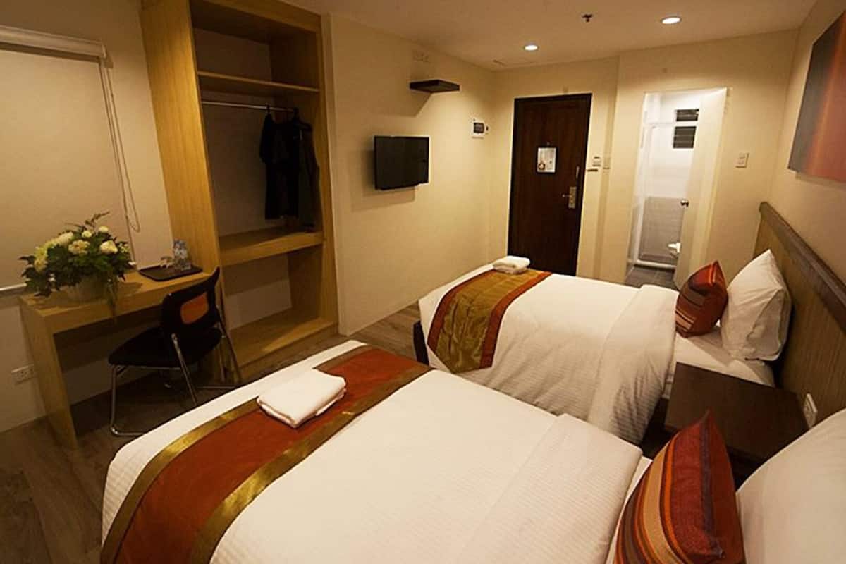 A hotel room with two beds, a desk, a chair, a TV, and a wardrobe.