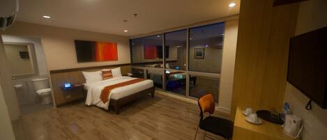 A hotel room with a bed, a desk, a chair, and a large window.
