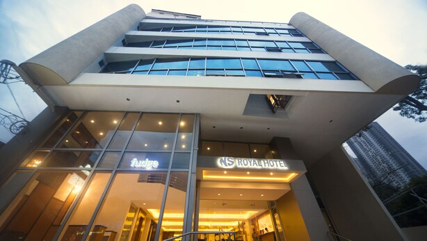 A modern hotel with a prominent "Royal Hotel" sign, large glass windows, and a staircase leading to the entrance. - NS Royal Hotel (Cebu City)
