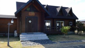 Une cabane en bois avec un toit sombre, une porte d’entrée et un petit porche avec des marches menant à l’intérieur.