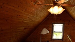 Une chambre confortable située sous les toits, avec deux lits, un ventilateur de plafond et une fenêtre laissant entrer la lumière naturelle.