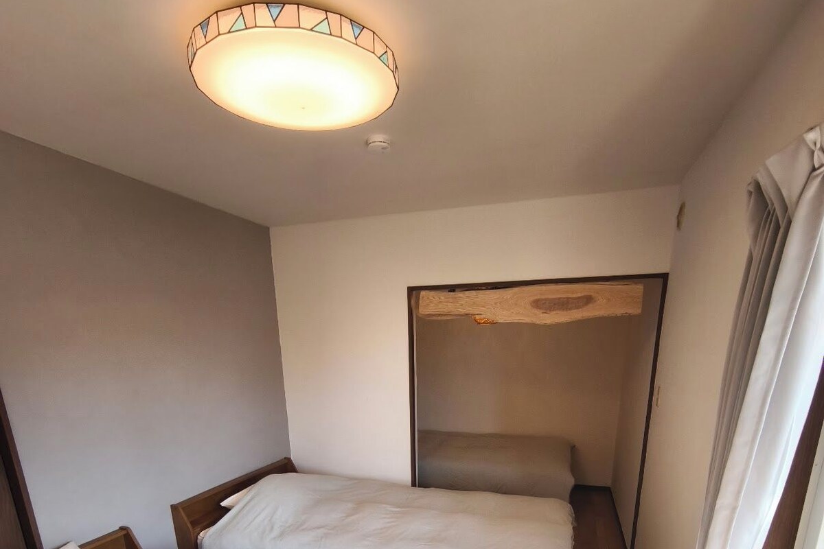 A room with two beds, a ceiling light fixture, and a window with curtains.