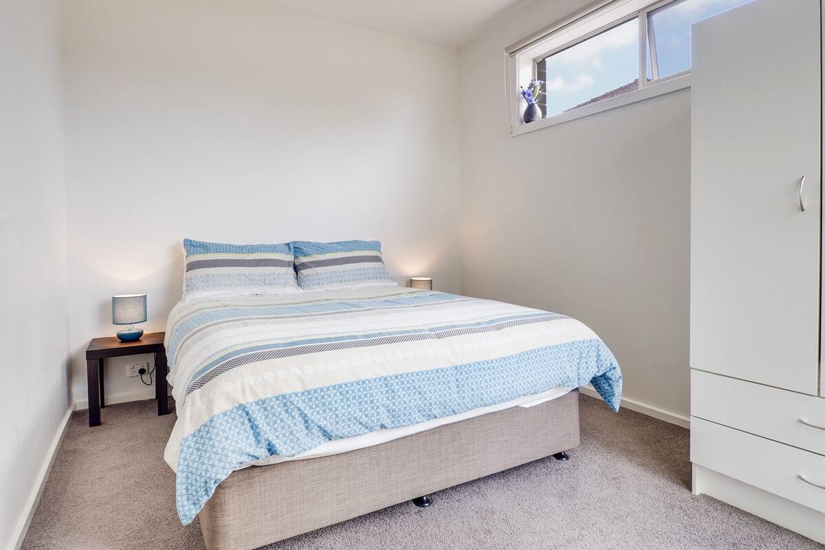 Ein Schlafzimmer mit Bett, Nachttisch, Lampe und Kleiderschrank.