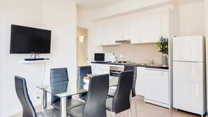 A modern kitchen with white cabinets, a microwave, stove, and a refrigerator. There is a glass dining table with four chairs.