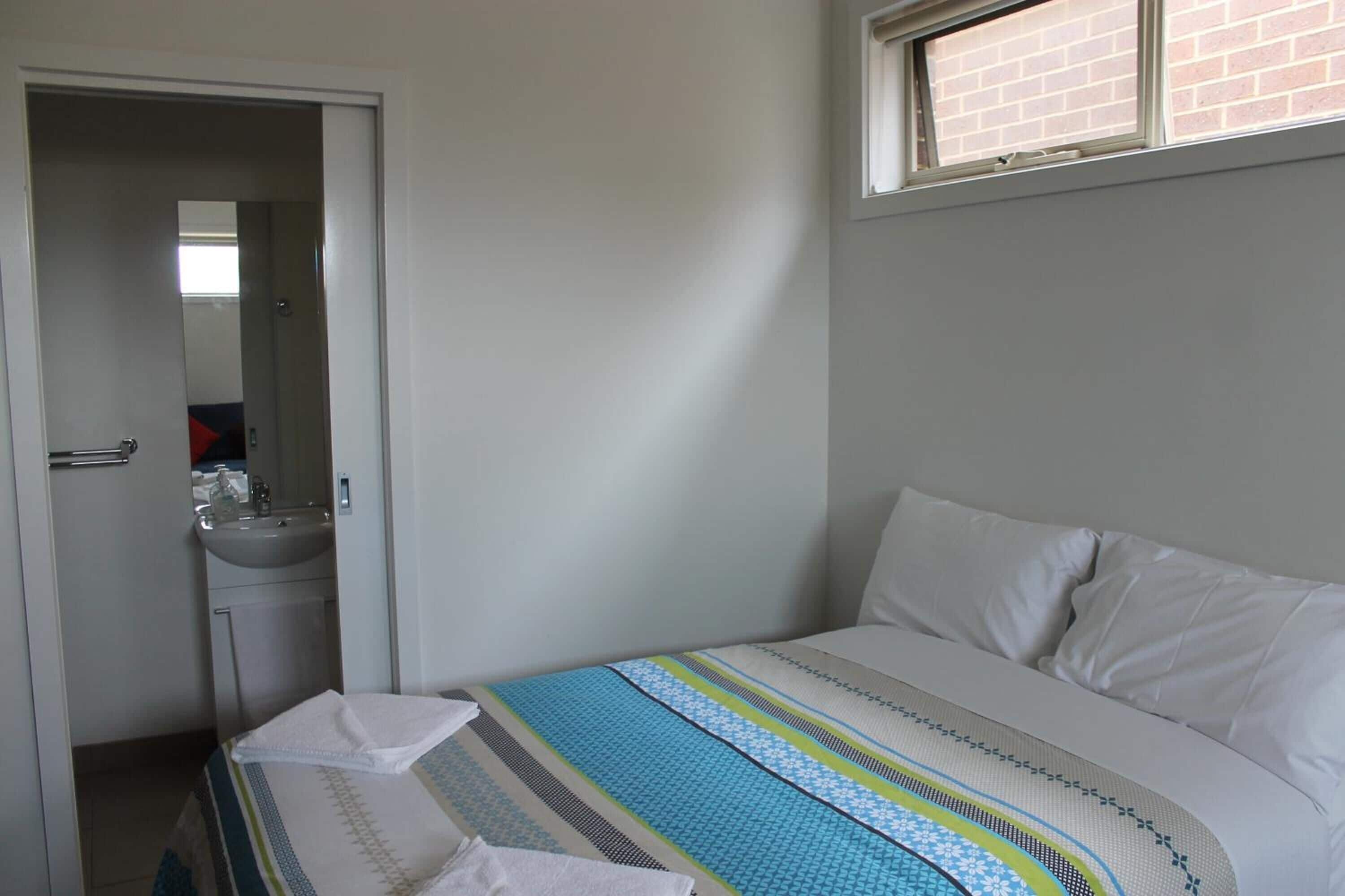 A bedroom with a bed, a window, and a bathroom visible through an open door.