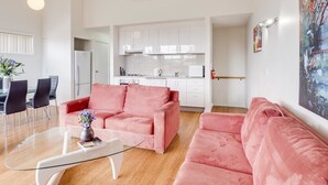 A modern living room with a pink sofa, a glass coffee table, and a dining area with a white table and chairs.