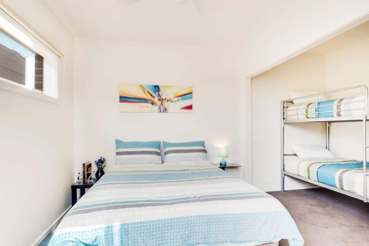 Ein Schlafzimmer mit einem Bett, einem Etagenbett, einem Deckenventilator, einem Nachttisch mit Lampe und einem Wandbild.
