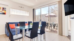 A modern living room with a glass dining table, blue sofa, and a flat-screen TV.