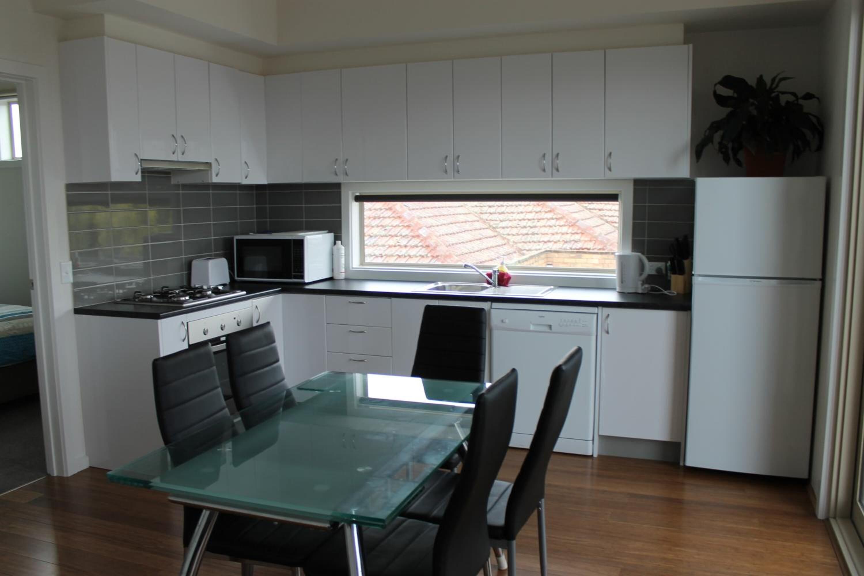 A modern kitchen with white cabinets, a glass dining table, and a view of the outside.
