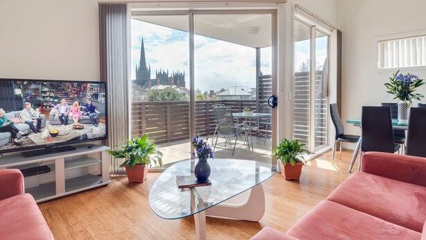 A modern living room with a television, seating, and a balcony with a city view.