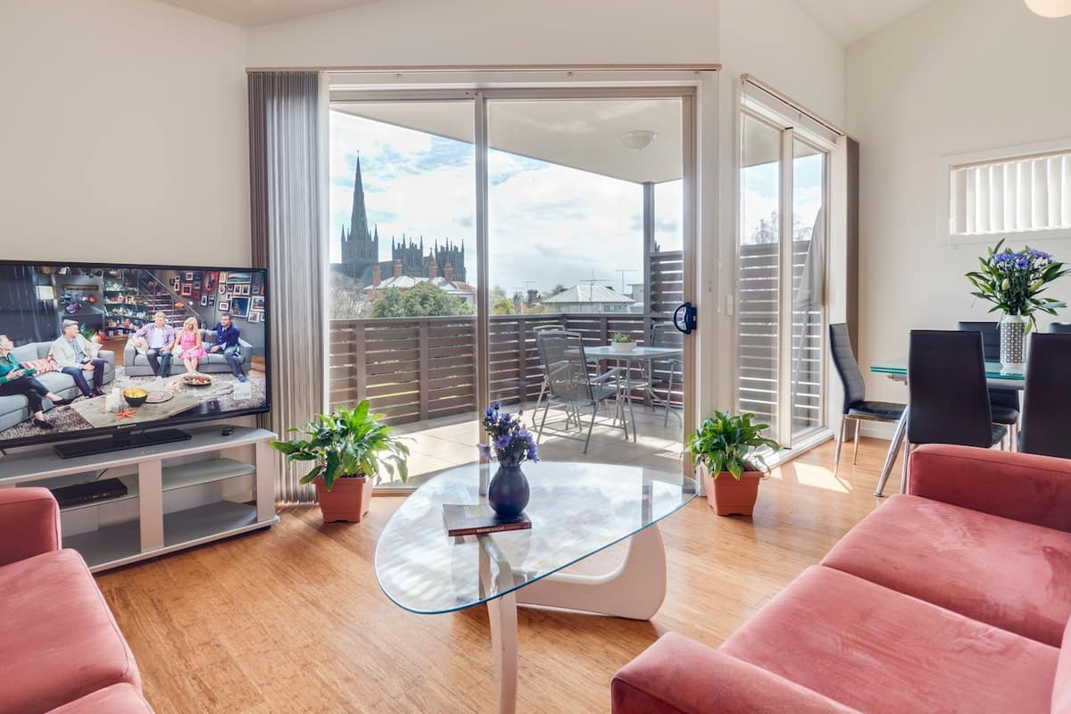 Ein modernes Wohnzimmer mit Fernseher, Sitzgelegenheiten und einem Balkon mit Blick auf die Stadt.