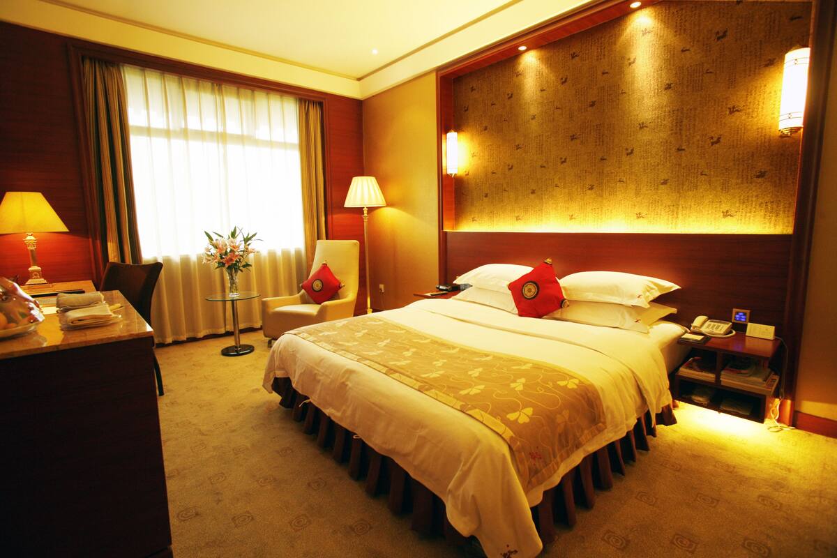 Ein Hotelzimmer mit einem großen Bett, Nachttischen, einem Schreibtisch, einem Stuhl und einer Lampe.