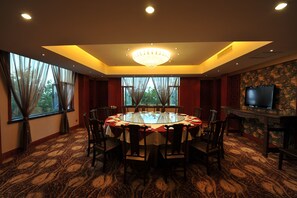 A conference room with a round table, chairs, a chandelier, and a television on a stone wall.