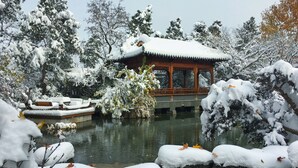 Un pavillon traditionnel surplombant un étang, entouré d’arbres et de rochers couverts de neige.