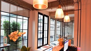 A modern office space with large windows, a desk with a computer, and hanging pendant lights. - Bedspread Hostel - Adults Only (Bangkok)