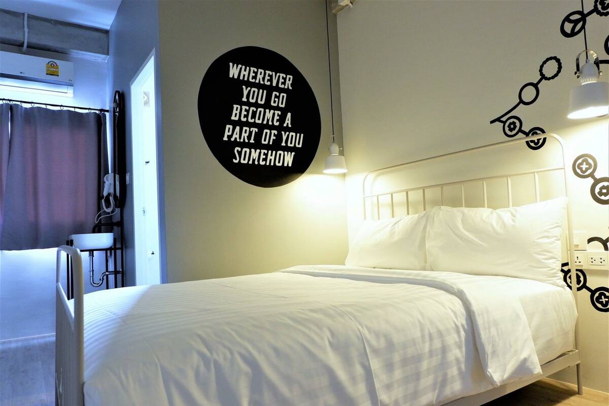 A neatly made bed in a hotel room with a motivational quote on the wall and a simple bedside table.