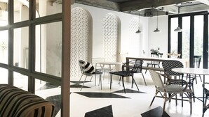 A modern dining area with a mix of metal and wooden furniture, large windows, and a geometric floor pattern. - Bedspread Hostel - Adults Only (Bangkok)