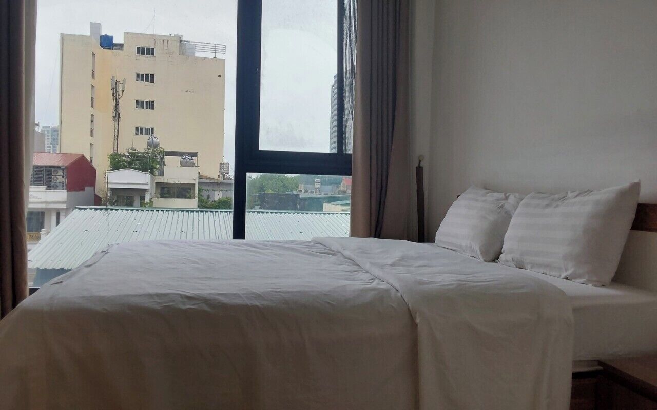 A hotel room with a large window, a bed with white bedding, and a view of a building outside.