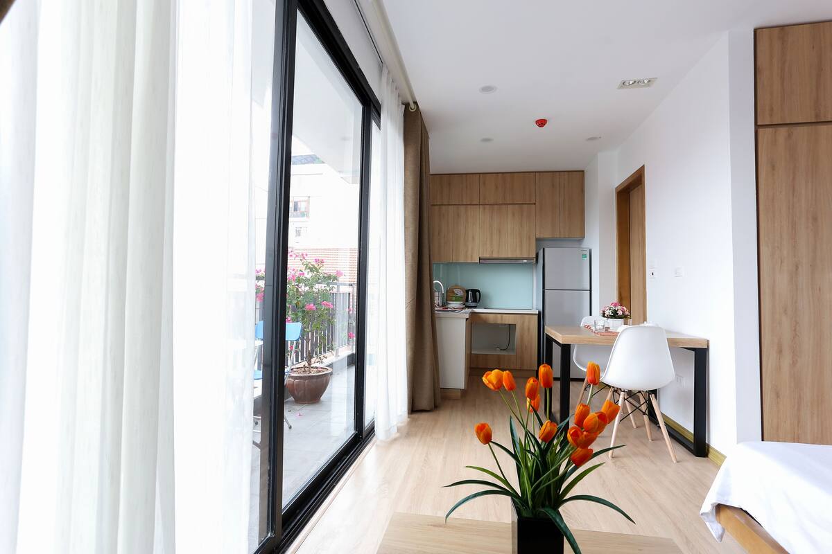 Habitació d'hotel moderna amb un finestral gran, zona menjador amb taula i cadires, i una cuineta.