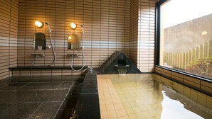A modern bathroom with a black bathtub, a shower area, and a window providing a view of the outside. - Kaisen no Yado Matsuura (Saiki)