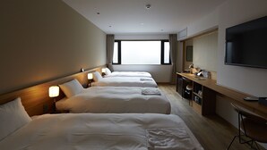 Una habitación de hotel con tres camas, un escritorio, un televisor y un ventanal grande.