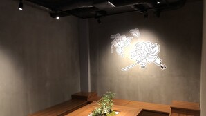 Un interior moderno con una mesa de madera y bancos, una planta pequeña e iluminación decorativa en la pared.