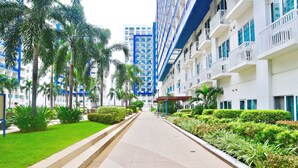 A modern hotel corridor with a central walkway, surrounded by lush greenery and palm trees. - CondoDeal at Sea Residences (Pasay)